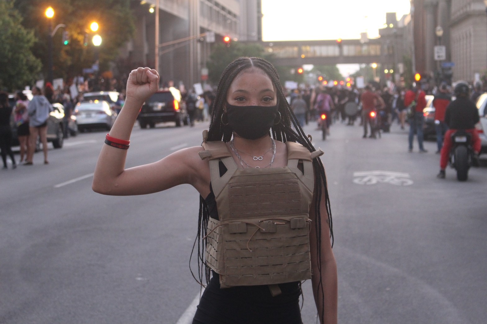 On May 29, 2020, a woman with her fist in the air stands on a street in Louisville, KY. Behind her crowds gather for a protest in support of Breonna Taylor.